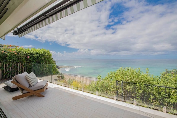 A balcony with a view of the ocean, a cushioned chair, and a wooden fence.