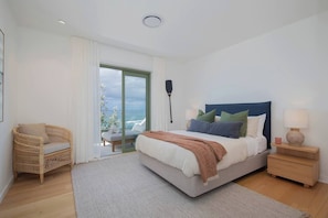 A bedroom with a bed, a chair, a nightstand, and a view of the sea.