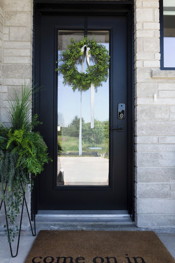 A black door with a doormat, a wreath, and a potted plant.