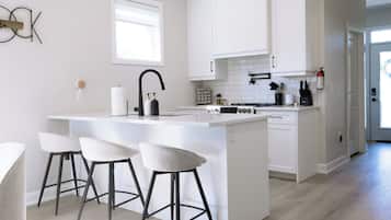A modern kitchen with a central island, bar stools, white cabinetry, and a window.