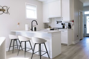 A modern kitchen with a central island, bar stools, white cabinetry, and a window.
