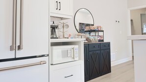 A kitchen with white cabinets, a microwave, a black cabinet, and a mirror.