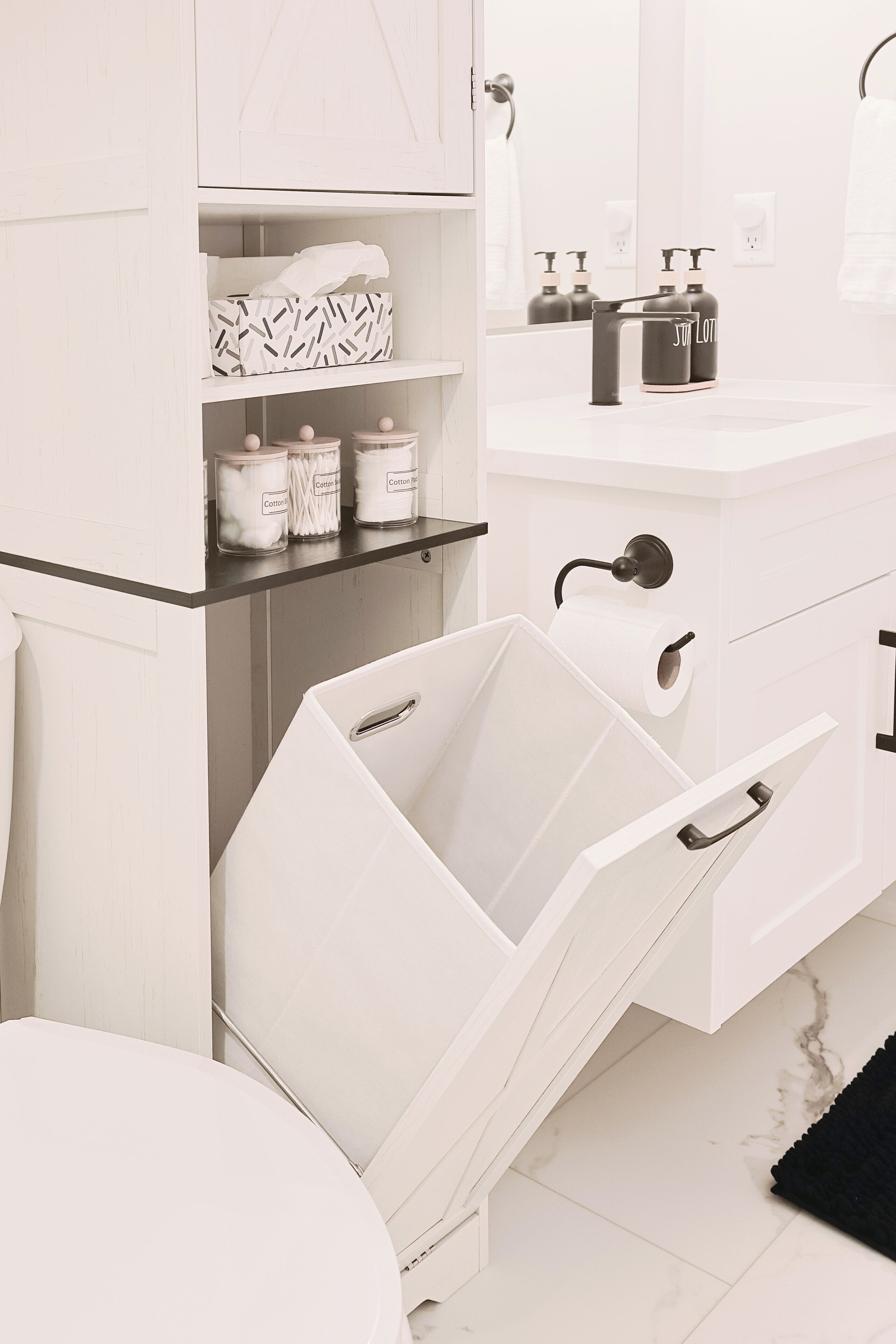 Een witte badkamer met een wit wastafelmeubel, een spiegel en een toilet. Er is een plankje met zakdoekjes en wattenstaafjes.