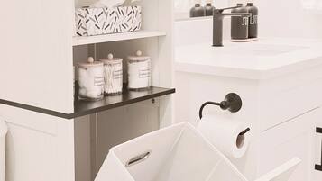 Een witte badkamer met een wit wastafelmeubel, een spiegel en een toilet. Er is een plankje met zakdoekjes en wattenstaafjes.