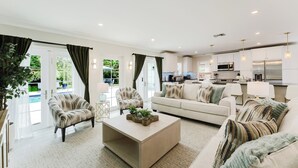 Una sala de estar moderna con un sofá, sillones, una mesa de centro y un área de cocina con armarios y electrodomésticos.