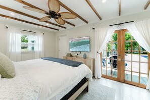 A bedroom with a bed, a ceiling fan, a TV, and a view of the outdoors. - Brand new 3 bedroom home with huge pool and garden (Lake Worth Beach)