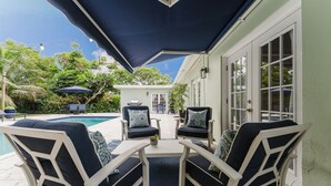 Un patio al aire libre con piscina, dos sillas con cojines estampados y una mesa.