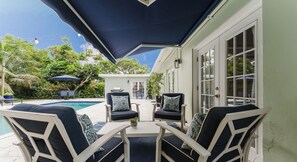 An outdoor patio with a pool, two chairs with patterned cushions, and a table. - Brand new 3 bedroom home with huge pool and garden (Lake Worth Beach)