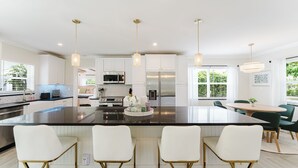Cocina moderna con armarios blancos, una isla grande con taburetes de bar, electrodomésticos de acero inoxidable e iluminación colgante.