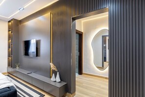 Et moderne hotelværelse med et fladskærms-tv, et konsolbord med dekorative genstande, et stort spejl og trægulv.