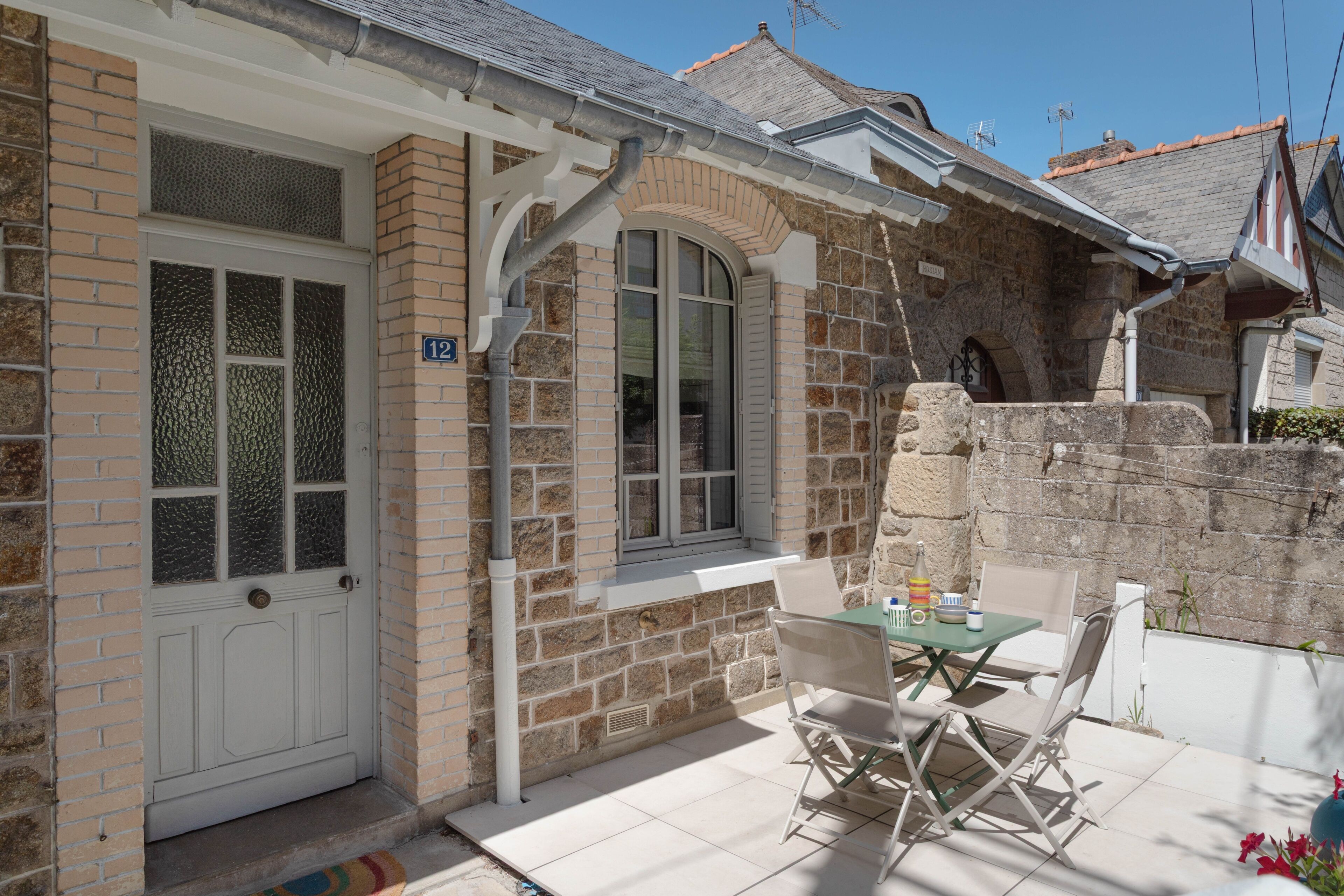 A stone house with a white door, a window, and a patio with a table and chairs.