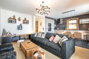 Ein modernes Wohnzimmer mit einer Couch, einem Couchtisch und einem Hund. Es gibt eine Küchenzeile mit einem Esstisch und Stühlen.