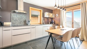 A modern kitchen with a dining area, wooden cabinets, a microwave, and a clock on the wall. - Les 3 Marmottes - Au pied des Pistes (Huez)