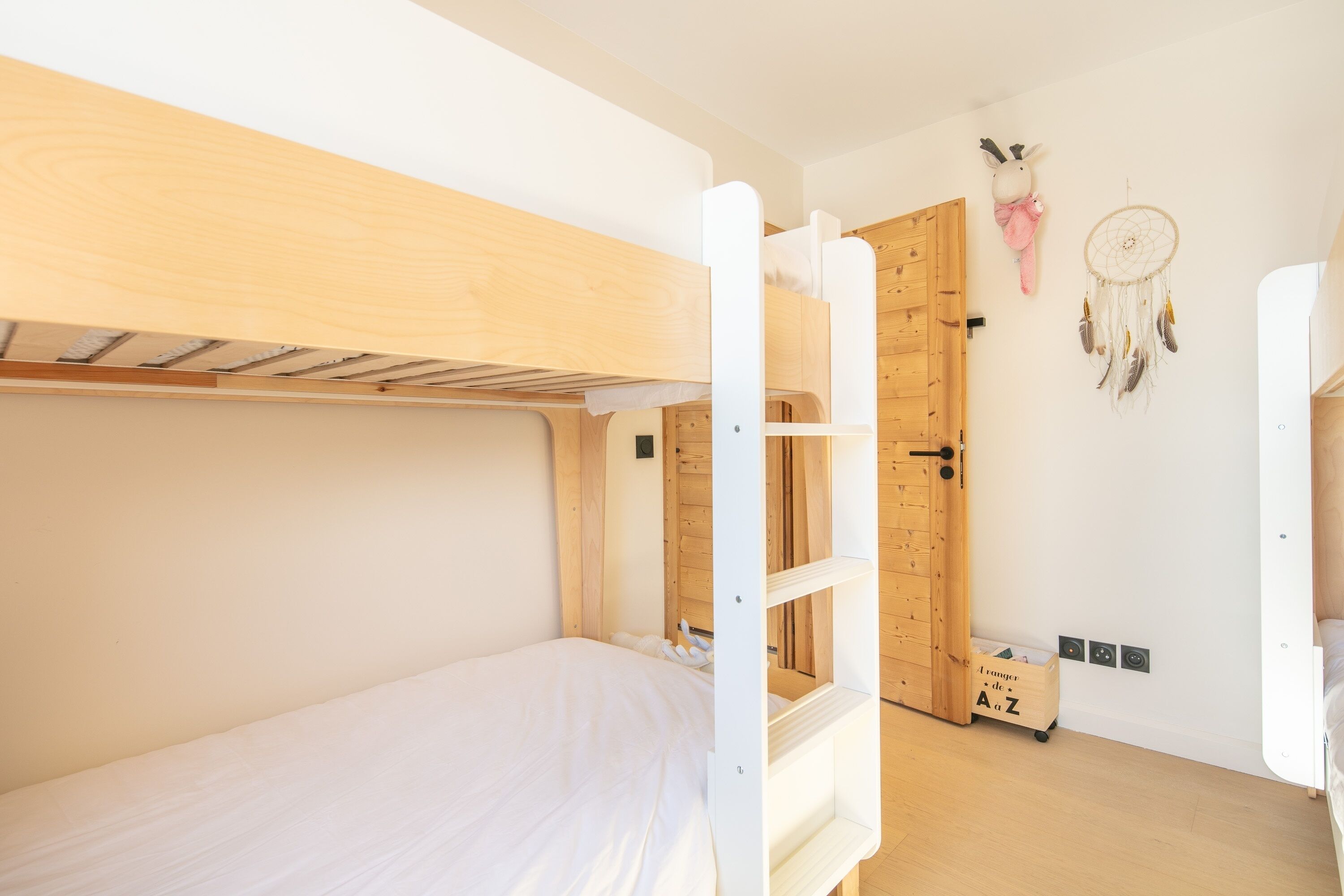 A bunk bed room with a wooden door, a dreamcatcher, and a storage box.