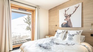 A bedroom with a large bed, a wooden headboard, and a wall-mounted deer artwork. - Les 3 Marmottes - Au pied des Pistes (Huez)