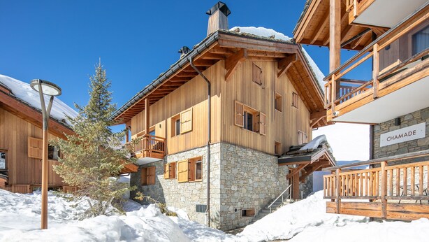 A wooden chalet with stone foundation, wooden balconies, and a sign reading 'CHAMADE'. - Les 3 Marmottes - Au pied des Pistes (Huez)