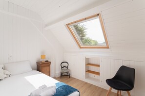 Et soveværelse med skrå vægge, ovenlys, seng, stol, natbord og lampe.