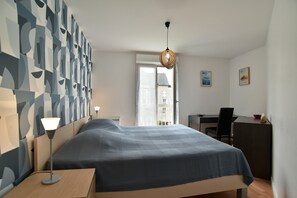 Un dormitorio moderno con cama, mesita de noche, lámpara, escritorio, silla y una obra de arte en la pared.