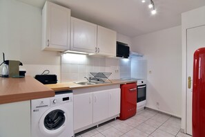 Una cocina compacta con armarios blancos, lavadora, lavavajillas rojo y microondas.