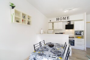 Une cuisine moderne avec des meubles blancs, une table à manger avec des chaises, un téléviseur à écran plat et une enseigne « HOME » placée au-dessus des meubles.