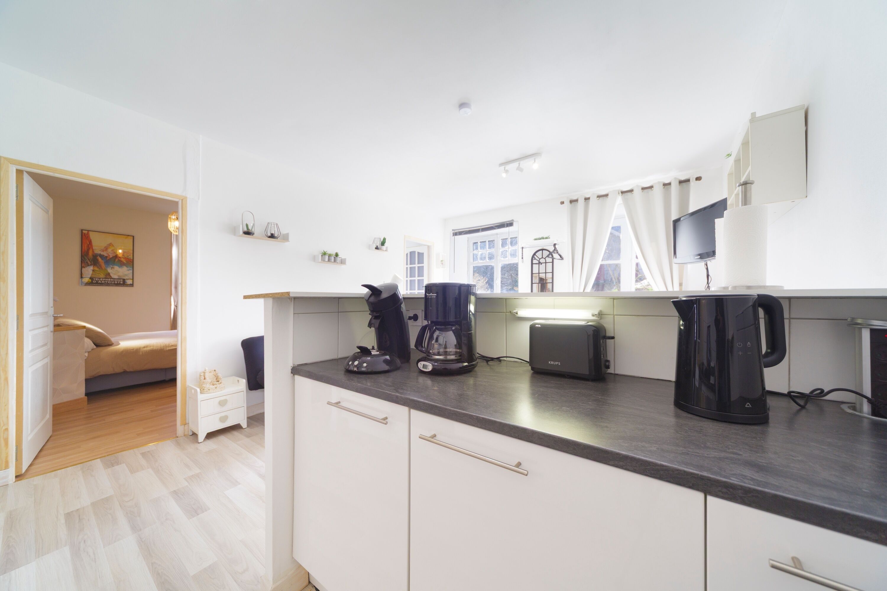 A modern kitchen with white cabinets, a coffee maker, and a kettle on the counter.