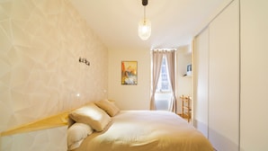 A bedroom with a bed, geometric wall design, a painting, and a window with curtains. - Le Gîte de Pount d'Iher - Proche GR10 (Laruns)