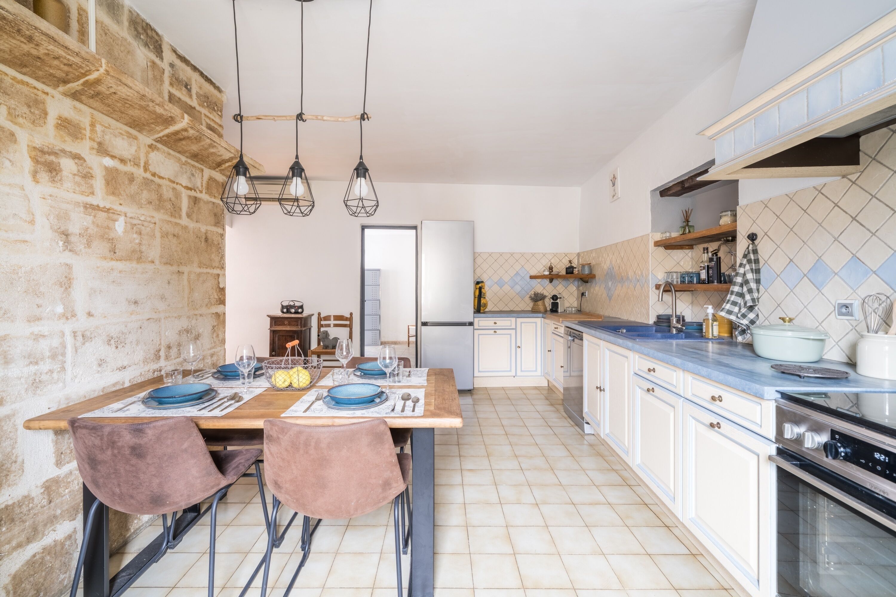 Eine Küche mit Ziegelwand, Holztisch und Stühlen, im Hintergrund ein Kühlschrank und ein Backofen.