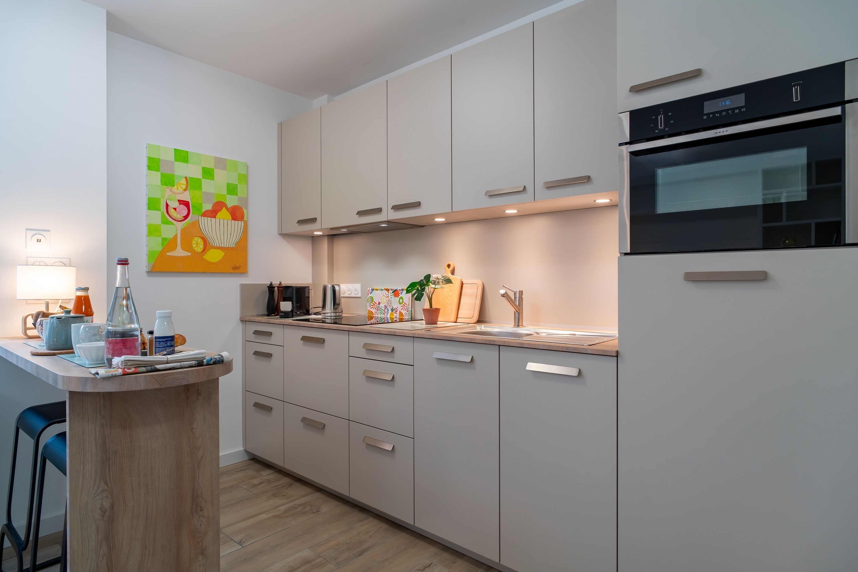 A modern kitchen with light-colored cabinets, a built-in oven, and a small island with stools.