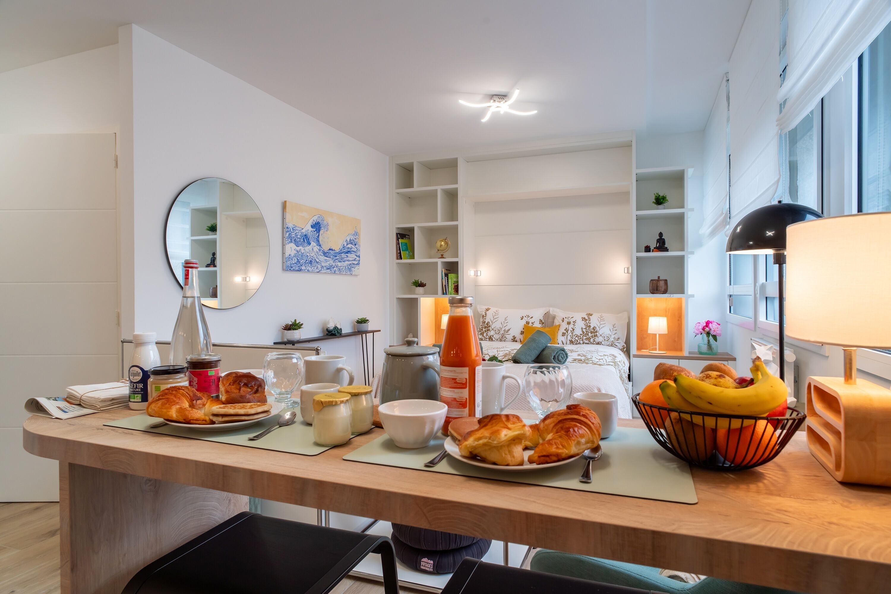 Eine moderne Küche mit Essbereich, mit einem Holztisch, Frühstücksgebäck, einem Spiegel und Blick zum Wohnzimmer.