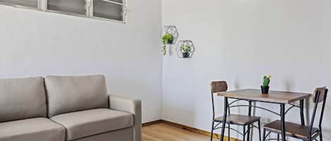 Une pièce avec un canapé beige, une table à manger en bois avec deux chaises, et deux jardinières hexagonales fixées au mur, contenant des plantes vertes.