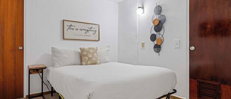 A bedroom with a bed, a bedside table, a wall-mounted light, and a decorative wall piece.