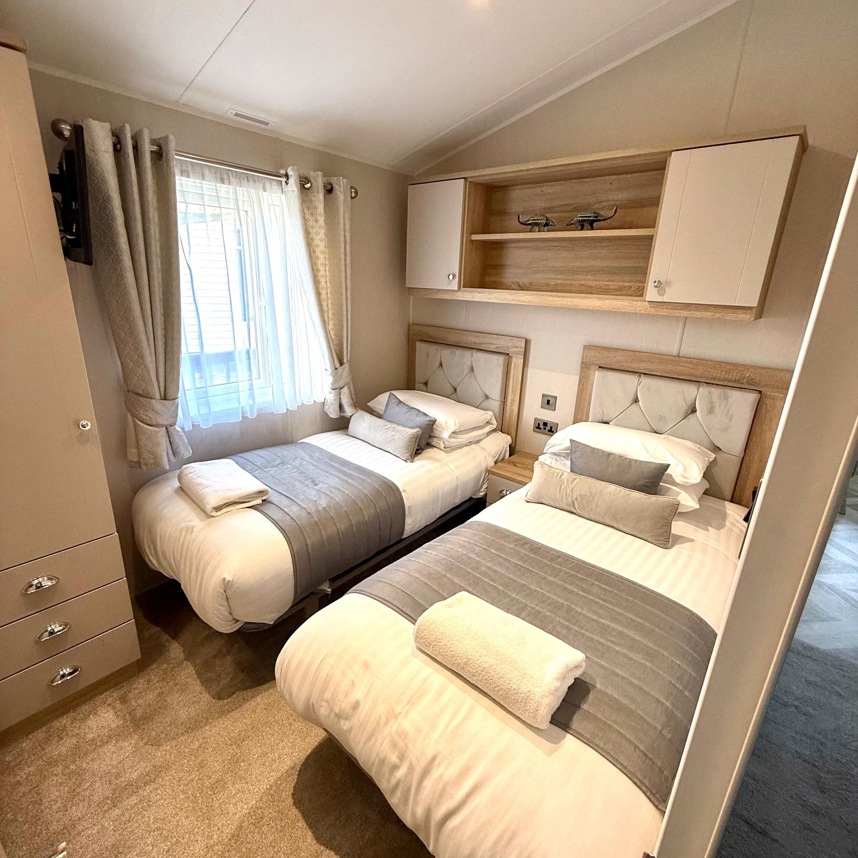 A bedroom with two beds, a wardrobe, a TV, and a window with curtains.