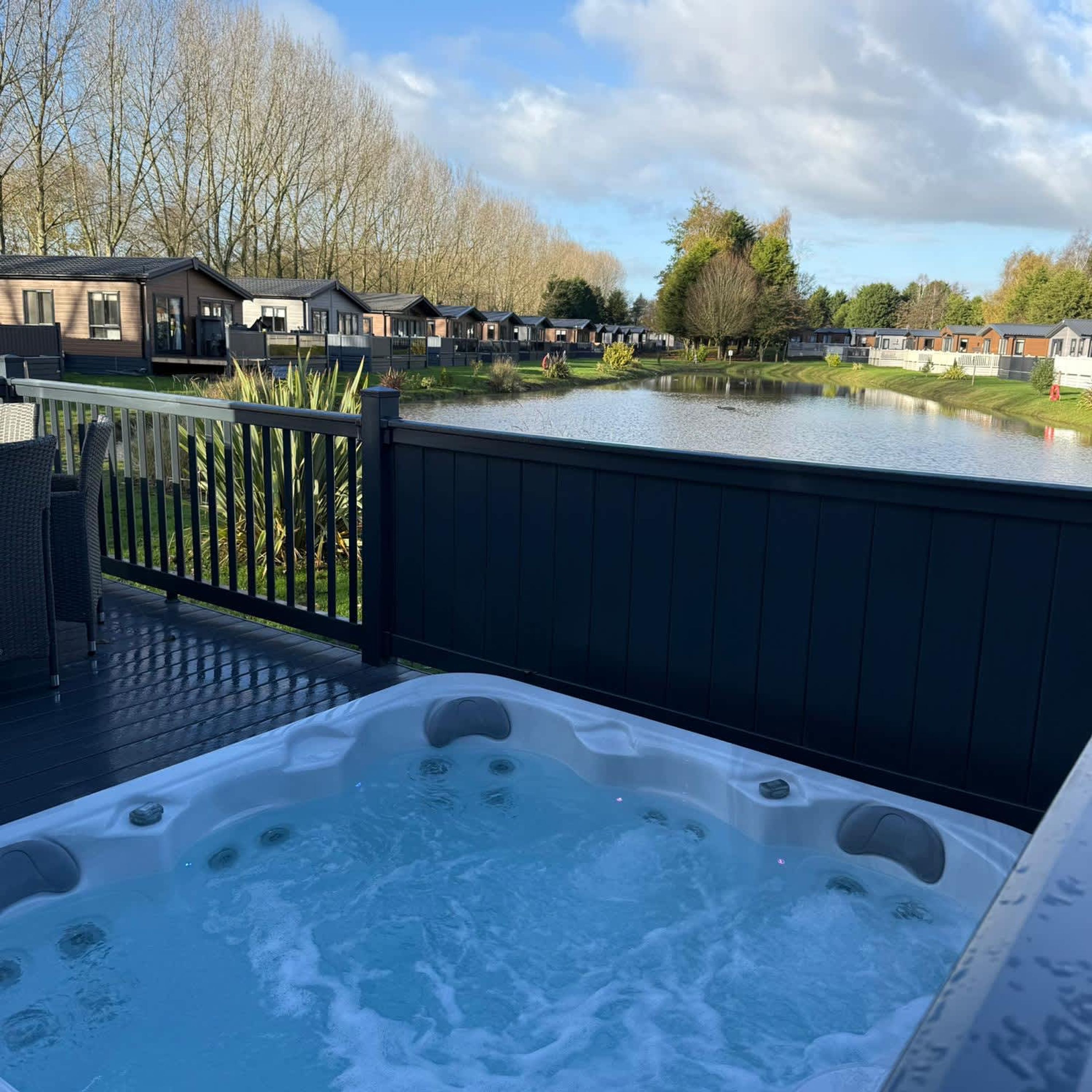 A hot tub on a deck with a view of a lake and row houses in the background.