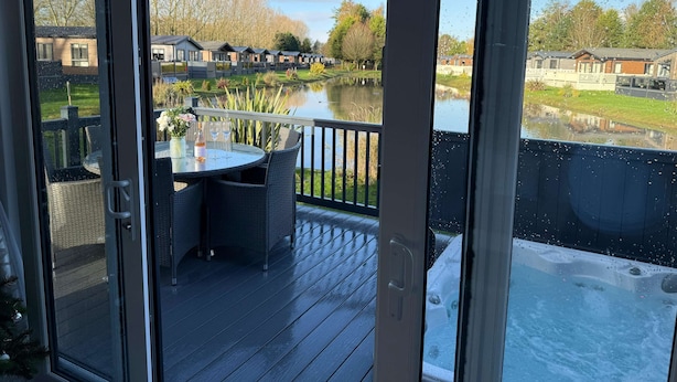 A covered outdoor area with a table and chairs, a hot tub, and a view of a lake and buildings. - Host Stay The White Swan (York)