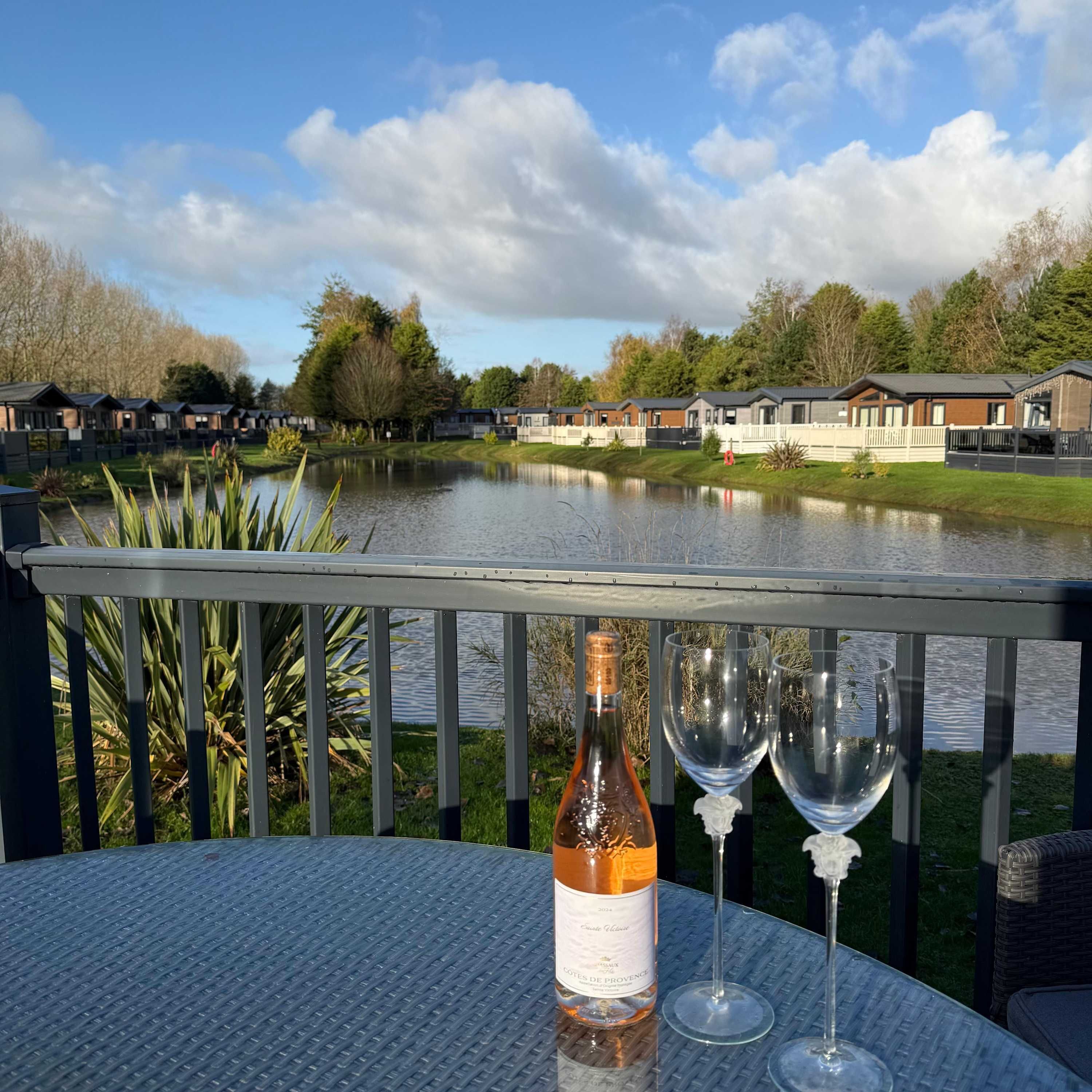 Vista sul lago con un tavolo, una bottiglia di vino e due bicchieri.