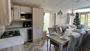 A modern kitchen with a gas stove, built-in oven, and microwave. There is a dining area with a wooden table and chairs, and a Christmas tree in the background. - Host Stay The White Swan (York)
