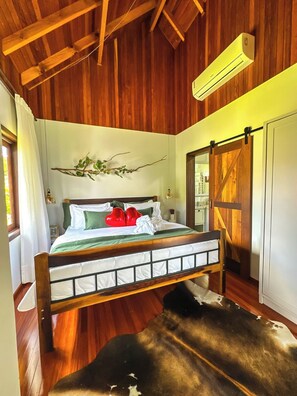 A wooden ceiling, a bed with pillows, a wall-mounted air conditioner, and a sliding barn-style door. - Morada Das Grimpas (Palmeira)