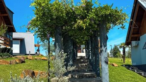 A stone pathway leading to a covered area with a pergola, surrounded by greenery and residential buildings. - Morada Das Grimpas (Palmeira)