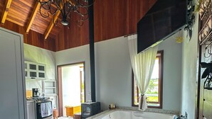 A spacious room with a large bathtub, wooden flooring, a hanging light fixture, and a view of the outdoors. - Morada Das Grimpas (Palmeira)