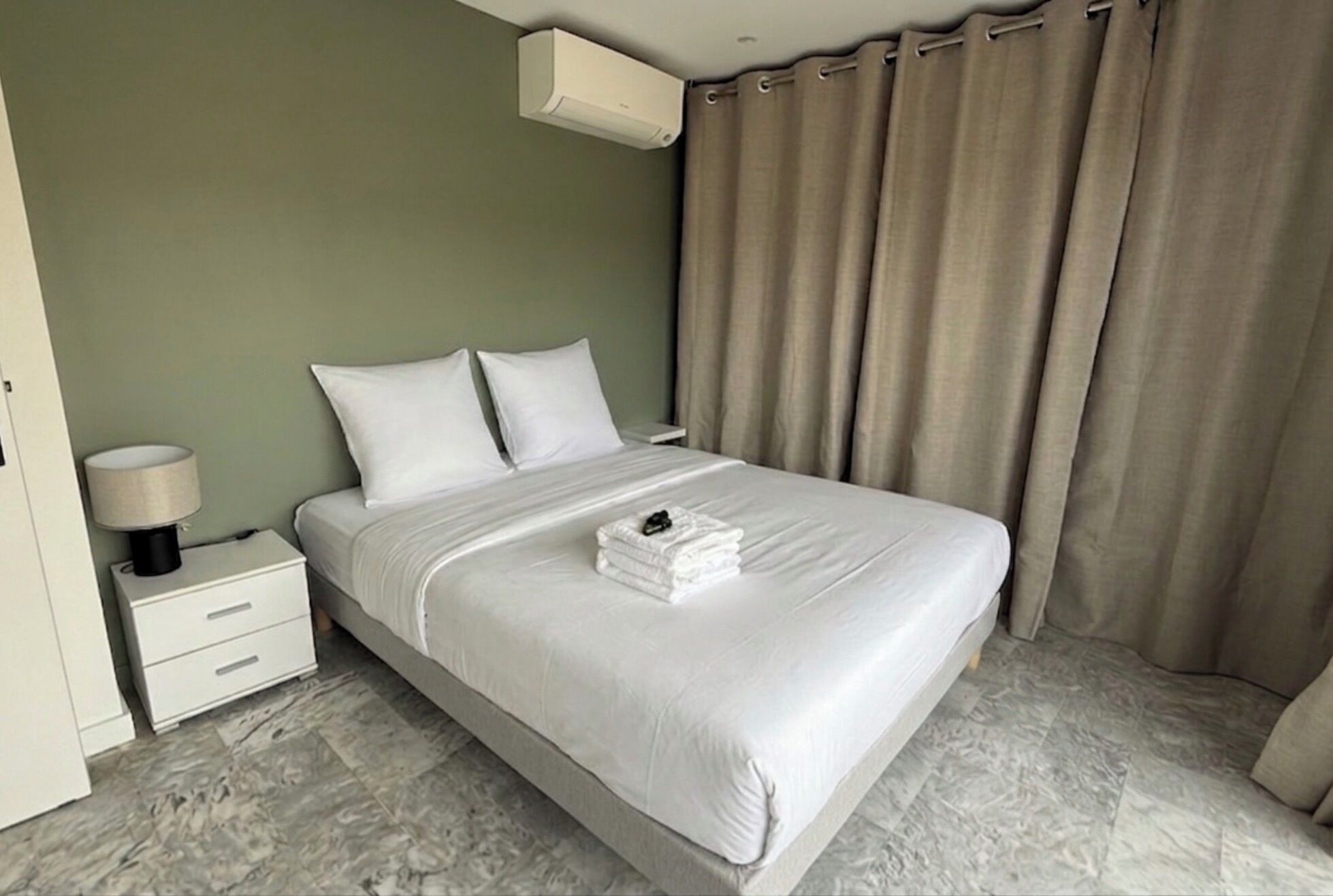 A neatly made bed with white linens, a bedside lamp, and a folded towel on the bed.