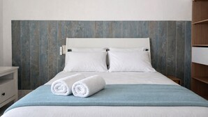 Un letto rifatto con lenzuola bianche e due cuscini, una coperta blu e due asciugamani arrotolati sul letto.