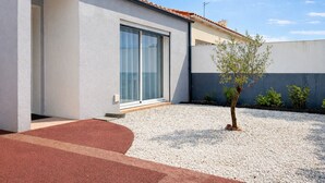 Un edificio moderno con un'ampia porta scorrevole in vetro, un piccolo albero nel vialetto e una strada di ghiaia.