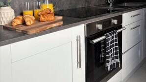 A modern kitchen with a black countertop, stainless steel appliances, and white cabinetry. - Home in Hotwells (Bristol)