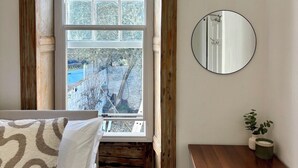 A bedroom with a large window, a wooden bench, a round mirror, and a small plant. - Home in Hotwells (Bristol)