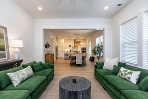 Ein geräumiges Wohnzimmer mit grünen Sofas, einem runden Couchtisch und einer Küche im Hintergrund.