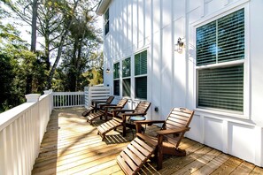 Eine Holzterrasse mit Gartenmöbeln, weißen Geländern und großen Fenstern mit Fensterläden.