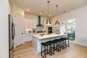 A modern kitchen with a central island, bar stools, pendant lighting, and a view to the outside. - 817 Cheehaw | Luxury Beach House | Sleeps 13 | Elevator | 1,000 ft to Beach Access | Dogs Welcome (Edisto Beach)