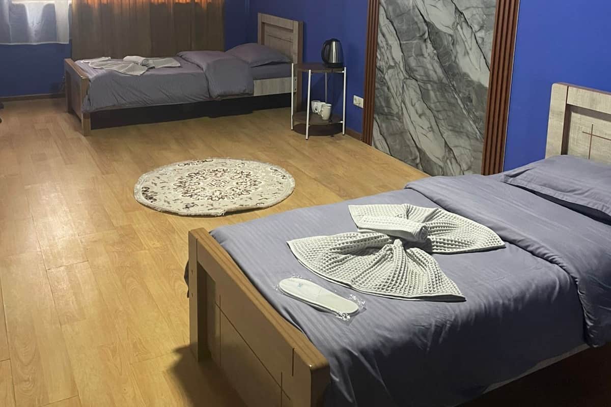 Une chambre avec deux lits, un plancher en bois, un mur en marbre et une fenêtre avec des rideaux.