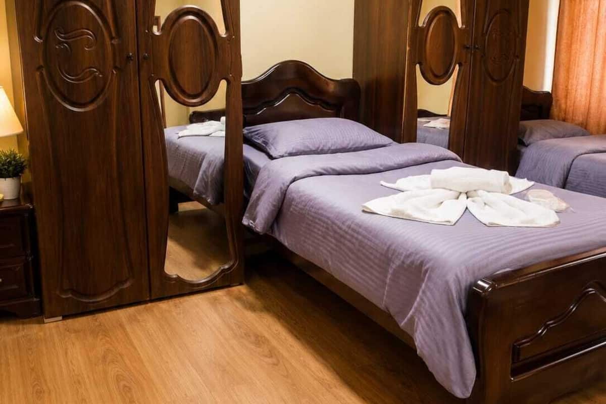 Une chambre avec un lit à baldaquin en bois, une armoire en bois et une table de chevet avec une lampe.