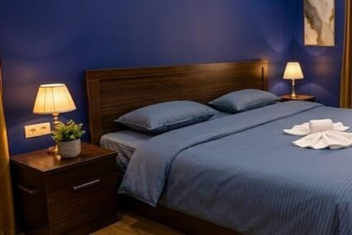Une chambre d’hôtel avec un lit, des lampes de chevet, une fenêtre donnant sur un beau paysage et une table de chevet avec une lampe.